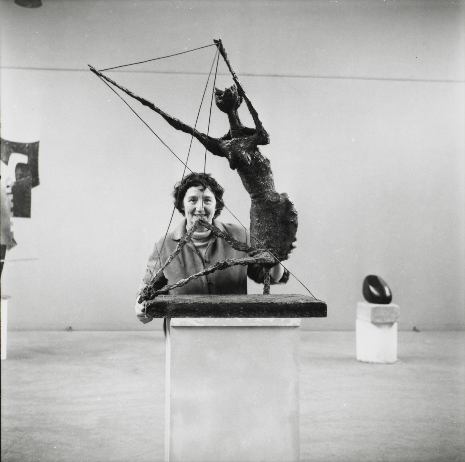 Photo en noir & blanc sur laquelle on peut voir Germaine Richier, souriante, derrière sa sculpture "La Fourmi" dans une salle d'exposition.
