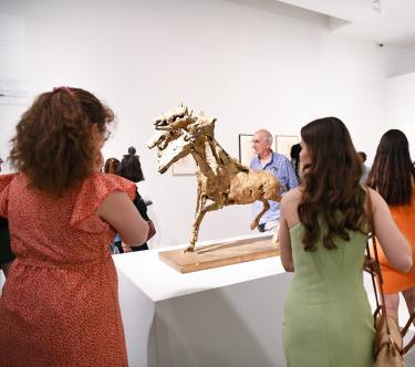 Dans une des salles de l'exposition Germaine Richier, plusieurs visiteurs regardent une sculpture représentant un cheval à six têtes en bronze doré.