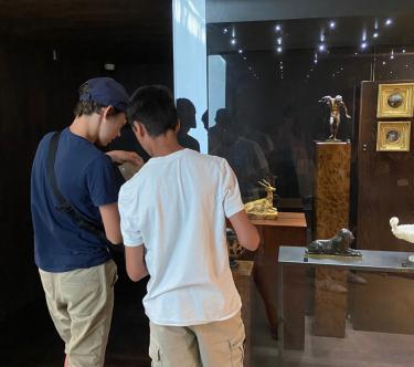 Devant une vitrine contenant plusieurs œuvres, on voit, de dos, deux adolescents.