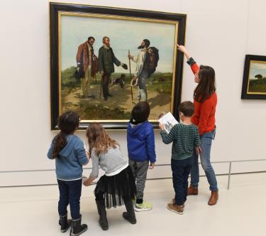 Une guide conférencière donne des explications à un groupe d'enfants devant le tableau Bonjour M. Courbet.