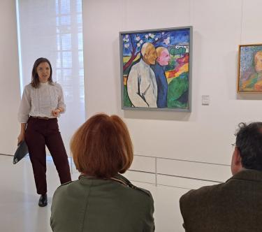 Dans une salle du musée, une médiatrice parle devant des visiteurs.