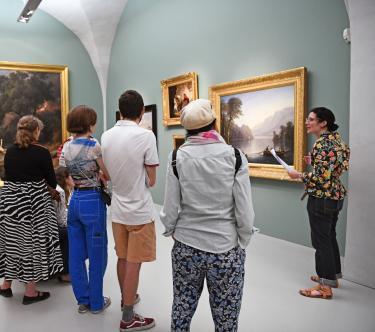 Dans une salle du musée, une guide, sur la droite, présente un tableau représentant un bâteau de pêche à un groupe de visiteurs.