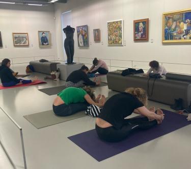 Dans une salle du musée, plusieurs personnes font des excercies de yoga sur des tapis de gymnastique.